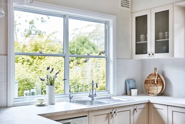 Interior photography of a fresh white Hamptons style kitchen with a marble bench top, large window looking out onto a back garden