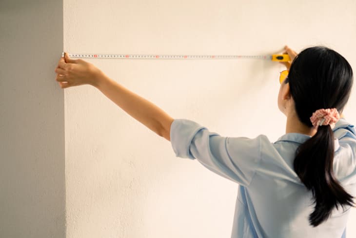 woman measuring wall with measuring tape