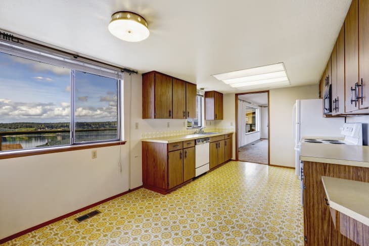 Empty kitchen room with linoleum floor, old storage cabinets and white appliances