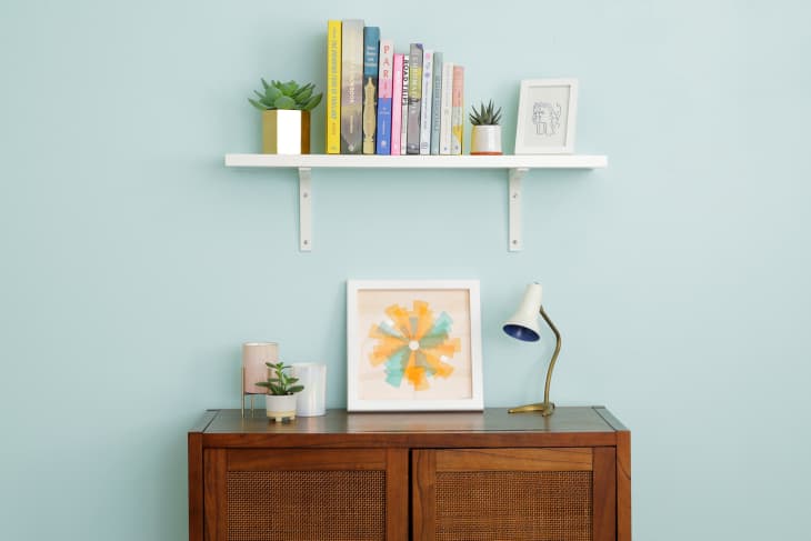 Installed bracketed wall shelf styled with books, plants and art.