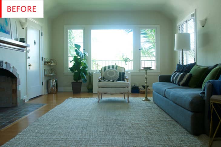 Living room with large window, gray sofa, white armchair, green plant, and fireplace.
