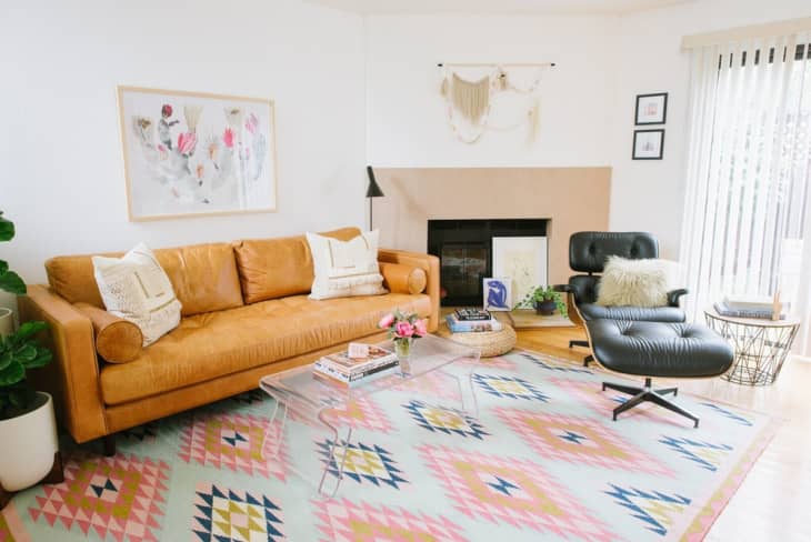Living room with tan leather sofa, black lounge chair, geometric rug, and wall art above a fireplace.