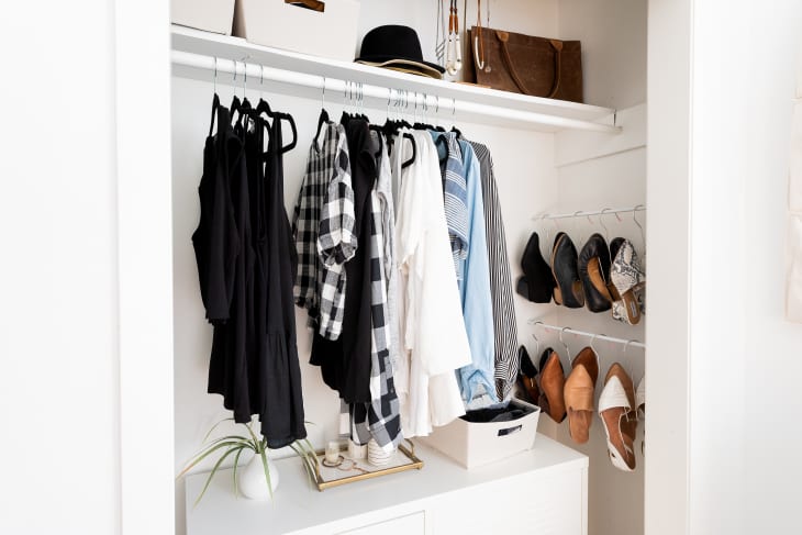 View of an open closet with a tension rods holding hangers of clothes and shoes