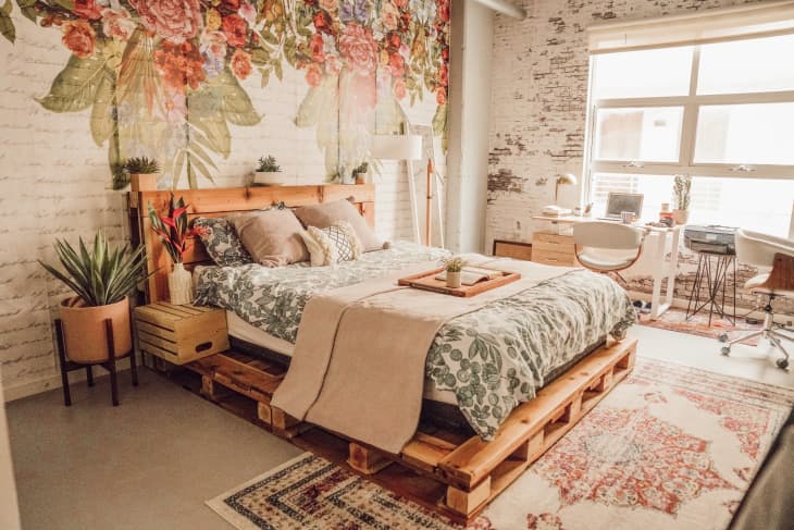 Industrial loft with wood pallet bed, floral accent wall, and exposed brick