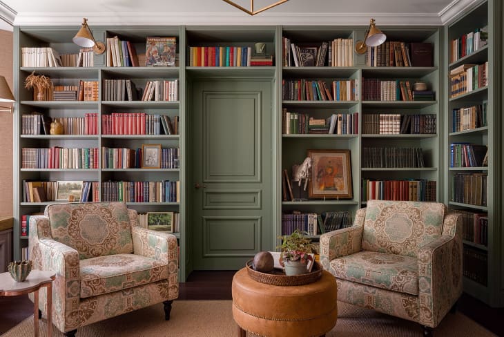 Sitting area with green wall-to-wall bookshelf, floral chairs, and round leather ottoman