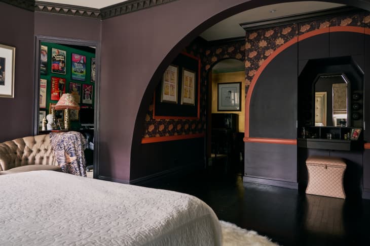 A purple bedroom with a curved wall; a different section of the room features black walls and a hexagon angled wall with a mirror