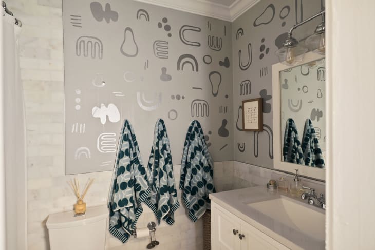 A bathroom with a funky mural and patterned hanging towels.