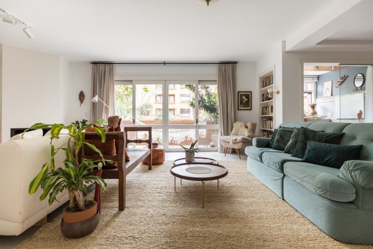 Spacious living room with a light blue sofa, wooden coffee table, large windows, and potted plants.