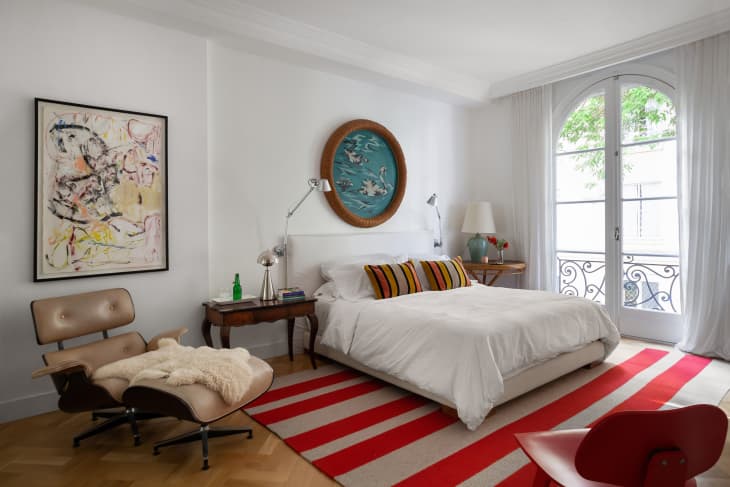 House tour in Buenos Aires, Argentina - bedroom. Bed has white linens, white fabric headboard. Striped rug, striped pillows on bed