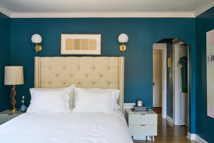 A bed with a tall upholstered headboard and sconces and an art piece above it