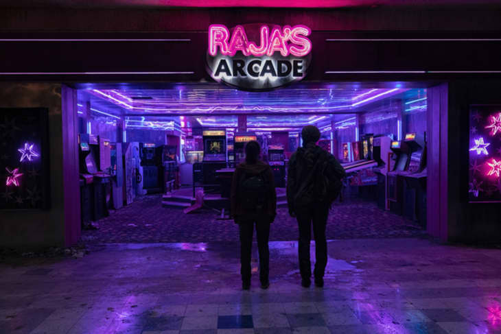 Two people standing outside Raja's Arcade, illuminated by neon lights, with various arcade machines visible inside.