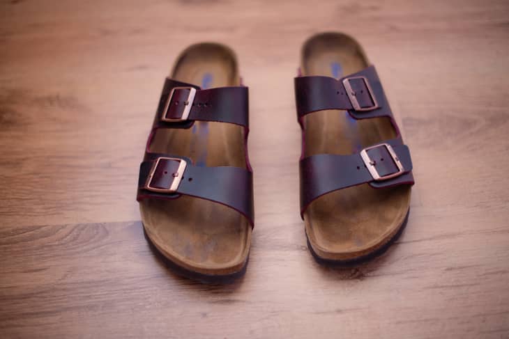 Brown leather sandals with two adjustable straps and buckles on a wooden floor.