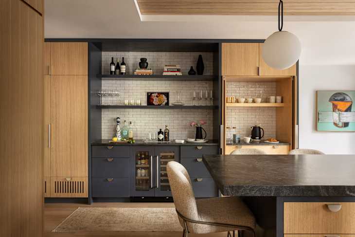 Modern kitchen with dark blue cabinetry, open shelves displaying glassware and bottles, and a large island with a dark countertop.