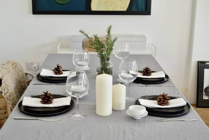 Nomita Vaish-Taylor's table set for a meal and using a wheat colored flat bed sheet as a tablecloth; closeup on the glasses and black plates with a pinecone as a place setting accent
