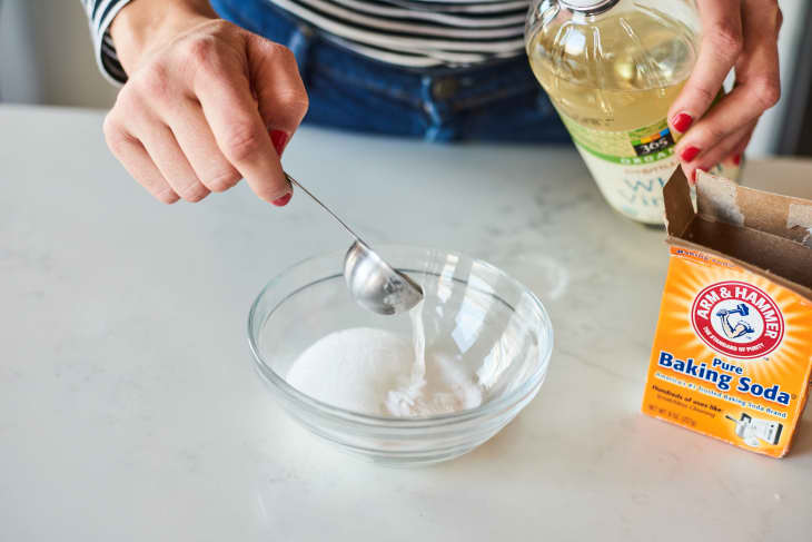 Mixing baking soda with vinegar in a glass bowl on a countertop.
