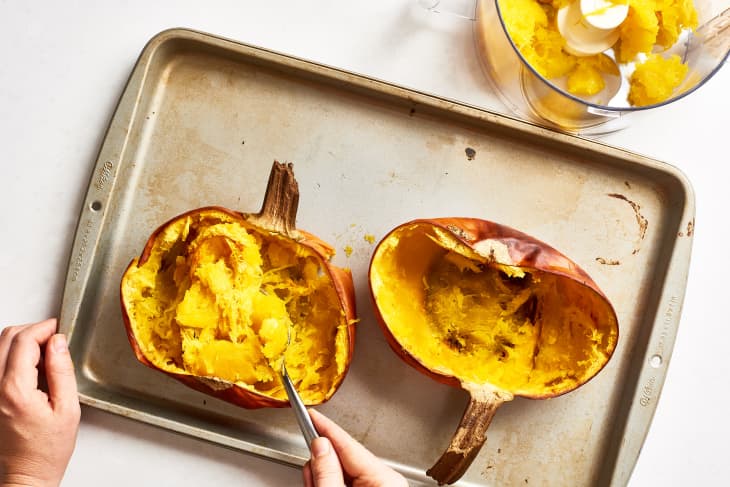 Image 4: A halved roasted pumpkin on a baking sheet, with one half being scooped out. A food processor with pumpkin purée is in the background.