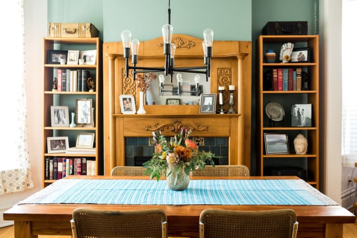 Dining room with wooden table, floral centerpiece, bookshelves, and decorative fireplace.