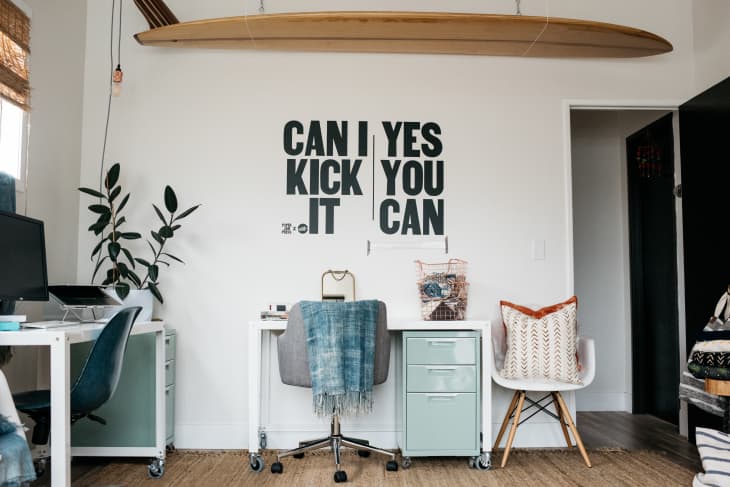 Home office with two desks, a surfboard on the wall, and motivational text art.