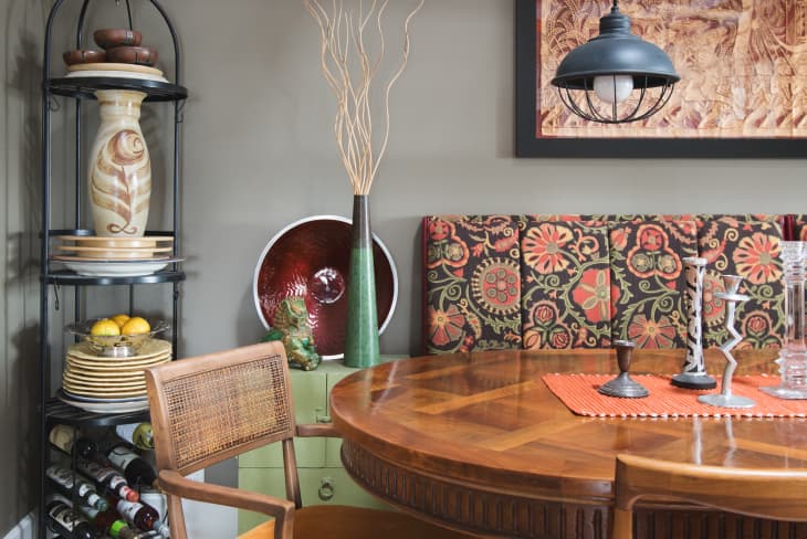 Dining area with patterned bench, round wooden table, decorative plates, and pendant light.