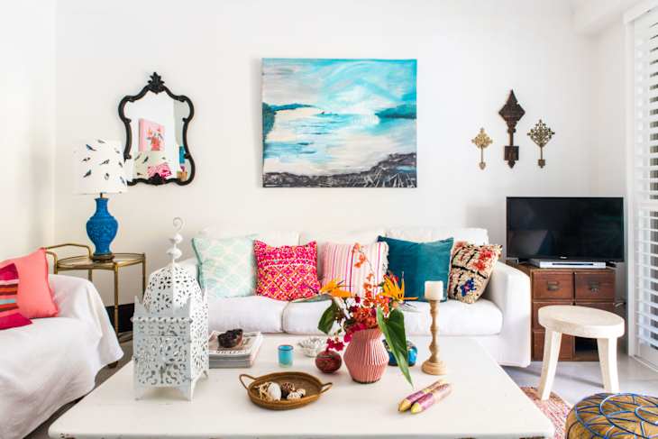 Living room with colorful cushions, abstract painting, ornate mirror, and decorative items on a white coffee table.