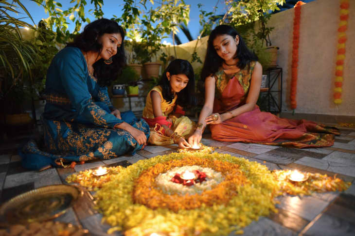 Mother and daughters lighting lamps around rangoli made using petals
