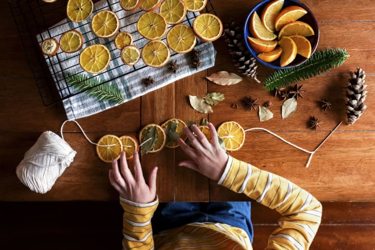 Childs hands putting together dried orange garland for Christmas