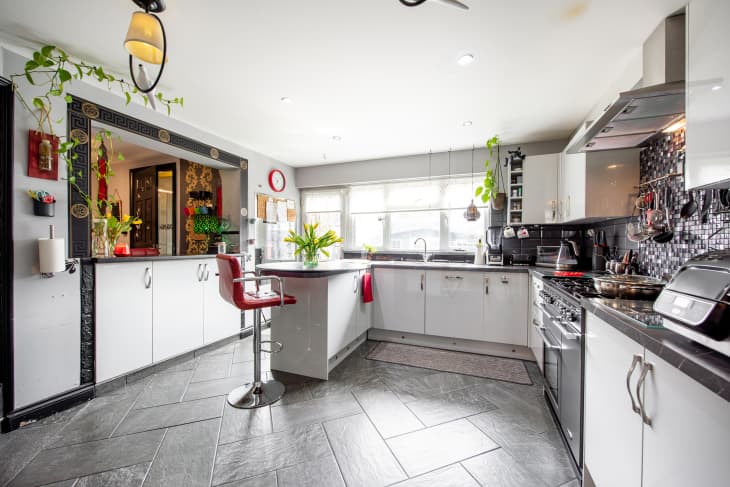 A general interior view of a white kitchen, red bar stool, grey range oven and novelty tropical bird light fittings