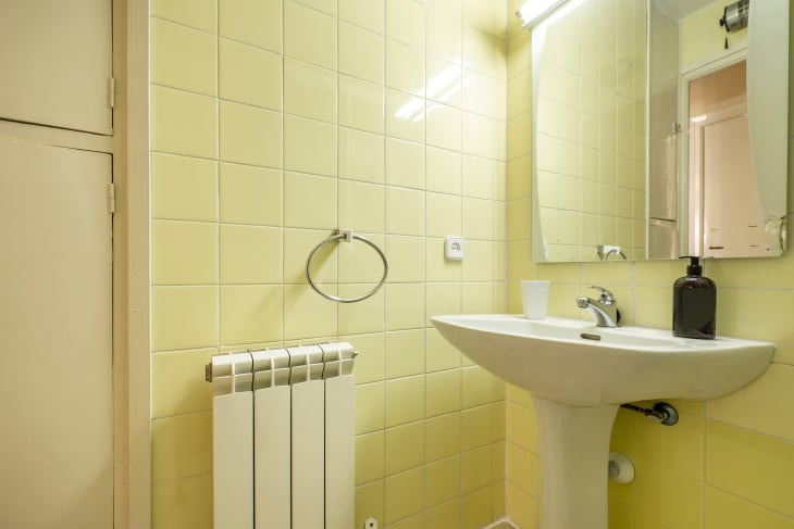 Bathroom with white wooden cabinets, glass-enclosed shower and square mirror above sink in vacation rental apartment