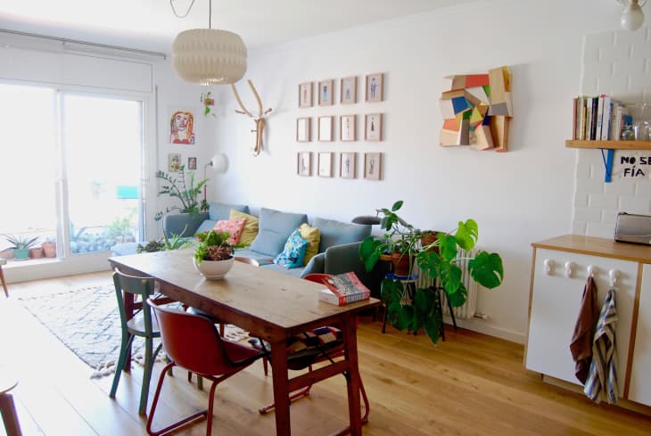 Living room with a wooden dining table, colorful chairs, gray sofa, wall art, plants, and a large window.