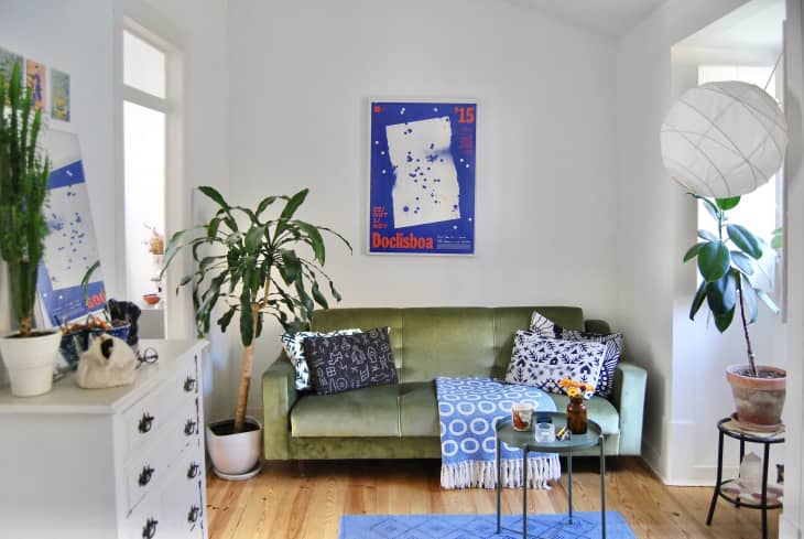 A white living room blue piece of art above a green couch and colorful rugs.