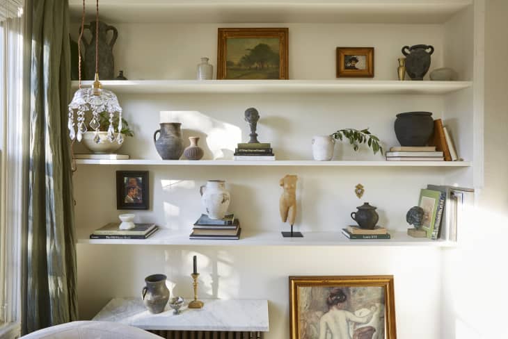 Bookshelf with decorative vases, sculptures, framed art, and books, next to a window with green curtains.