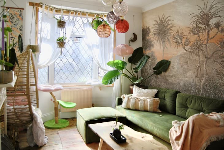 Living room with green velvet sofa, large windows with hanging plants, colorful glass globe pendant lights, wall with natural landscape mural