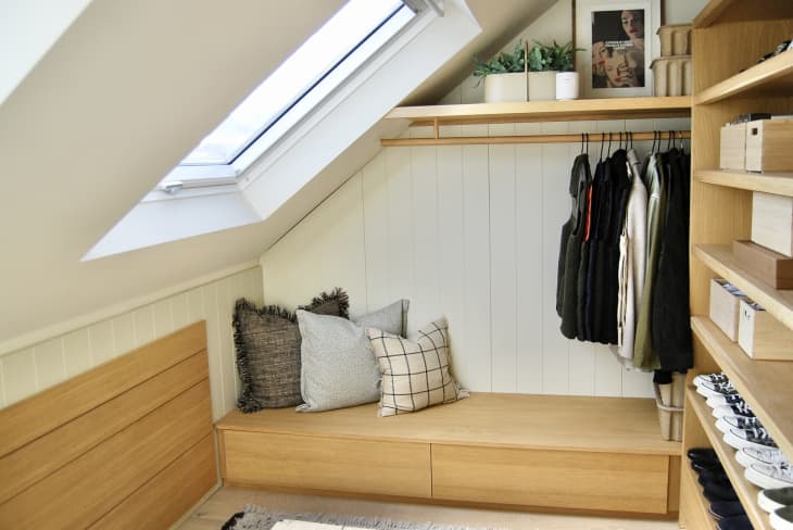 walk in closet with angled ceiling, skylight, wood slat doors, lots of wood details, hanging racks, bench with pillows