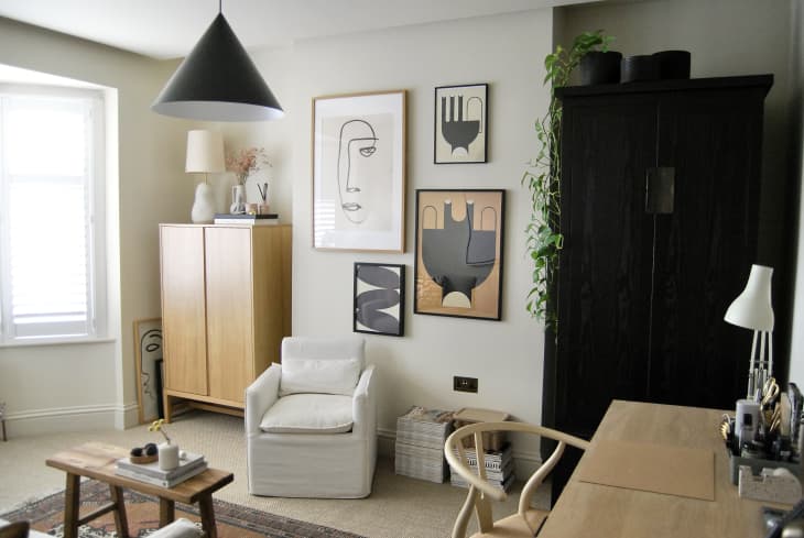home office with pale gray sofa, lots of modern framed art, black pendant lamps, light wood furniture, natural rug with smaller patterned area rug