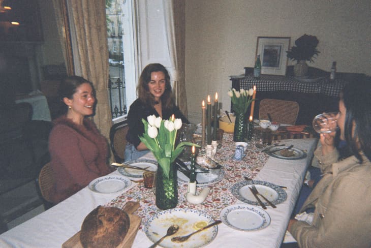 Dinner party table with tablecloth, nice place settings, lit candles, vase of tulips. people at the table after eating, chatting