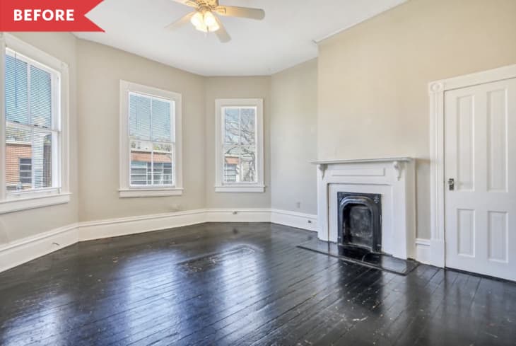 Before: Large room with three windows, black floors, beige walls, and old fireplace