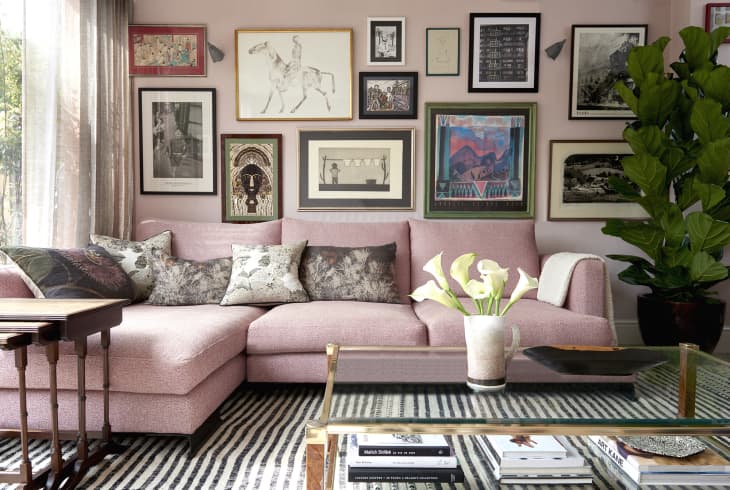 Pink sofa with floral cushions, gallery wall art, glass coffee table, and large potted plant in a cozy living room.