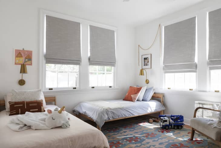 Children's bedroom with two beds, gray blinds, colorful rug, unicorn plush, and toy truck.