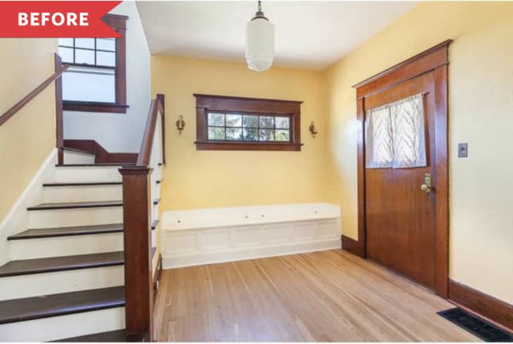 Entryway with wooden staircase, yellow walls, wood door, and a white bench under a window.