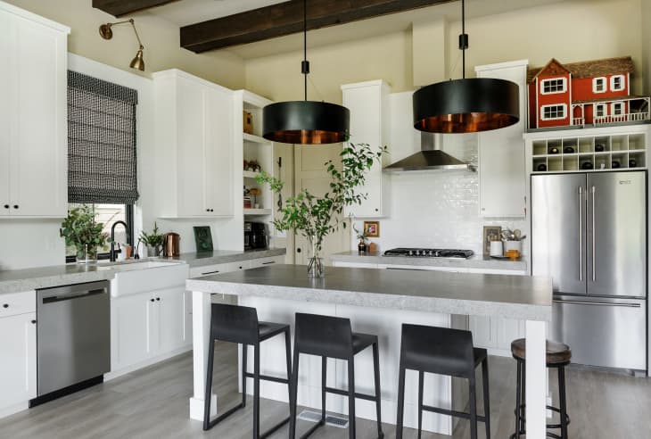 Modern kitchen with white cabinets, stainless steel appliances, black pendant lights, and a large island with bar stools.