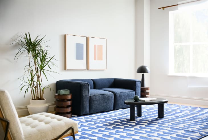 Living room with blue sofa, white walls, art over sofa, natural color armchair, Marimekko/West Elm collab blue and white patterned rug