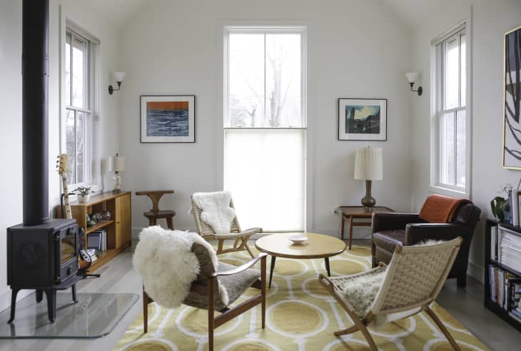 Cozy living room with mid-century chairs, round table, wood stove, and abstract art on white walls.