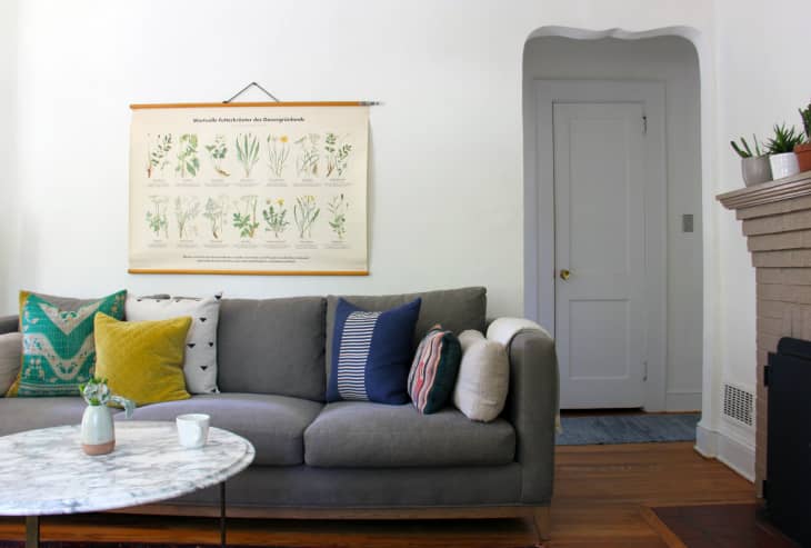 Gray sofa with colorful pillows, marble coffee table, botanical wall art, and a brick fireplace in a cozy living room.