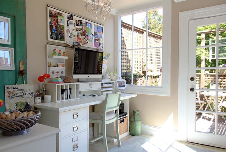 Home office with white desk, computer, photo board, and French doors leading to a sunny patio with a table and chairs.
