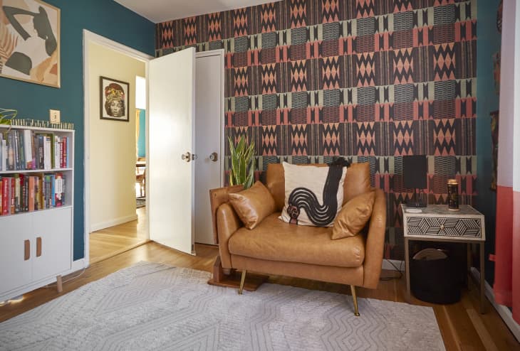 Room with patterned wallpaper, tan leather chair, bookshelves, area rug