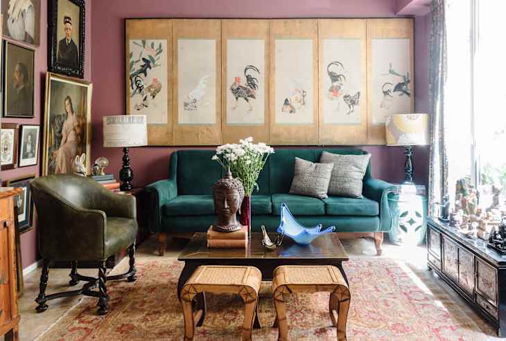 Eclectic living room with green sofa, vintage art, Buddha statue, and floral decor on a patterned rug.