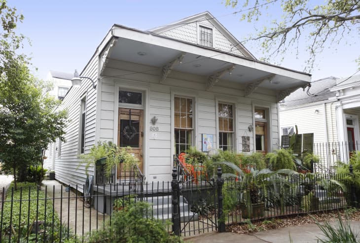 Historic white house with a front porch, ferns, and iron fence, located in a residential neighborhood.