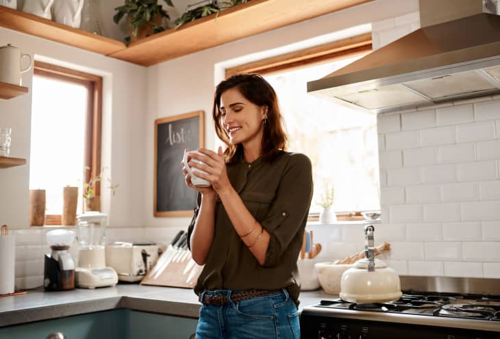 woman having a cup of coffee while standing in her kitchen at home