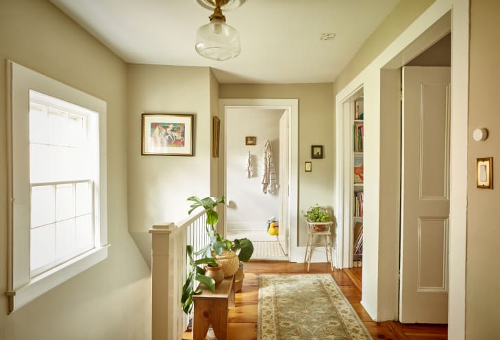 Hallway with a potted plant on a wooden bench, framed art, and a view into a bathroom with hanging towels.