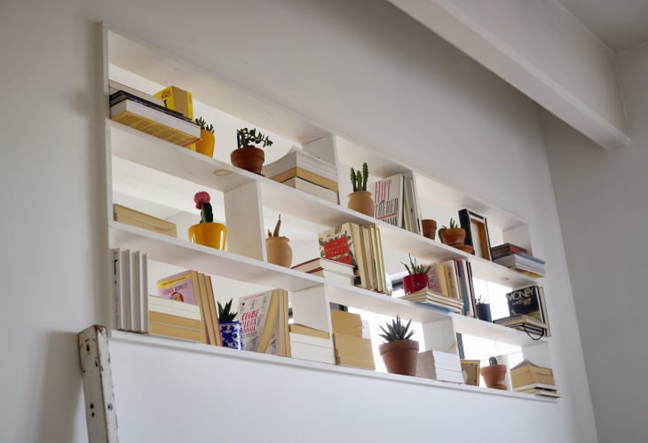 Wall-mounted white bookshelves with assorted books, potted plants, and decorative items.